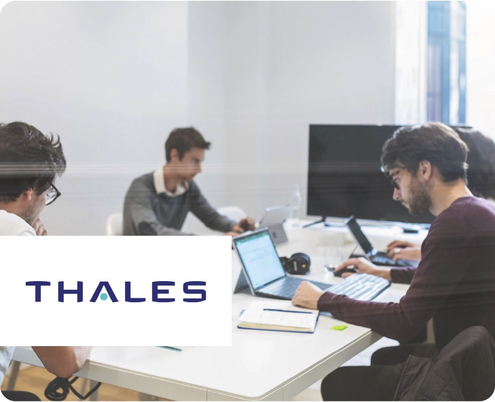 Some people working in an office environment. Thales logo at the front.